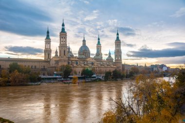 Fotoğraf, gün batımında Zaragoza şehrindeki Ebro nehri üzerindeki Basilica De Nuestra Senora del Pilar 'ın yanındaki taş köprüden. İspanya