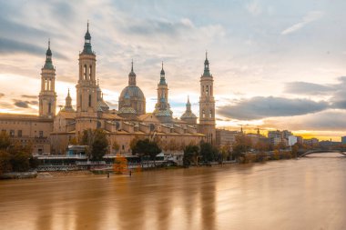 Fotoğraf, gün batımında Zaragoza şehrindeki Ebro nehri üzerindeki Basilica De Nuestra Senora del Pilar 'ın yanındaki taş köprüden. İspanya