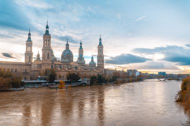 Fotoğraf, gün batımında Zaragoza şehrindeki Ebro nehri üzerindeki Basilica De Nuestra Senora del Pilar 'ın yanındaki taş köprüden. İspanya