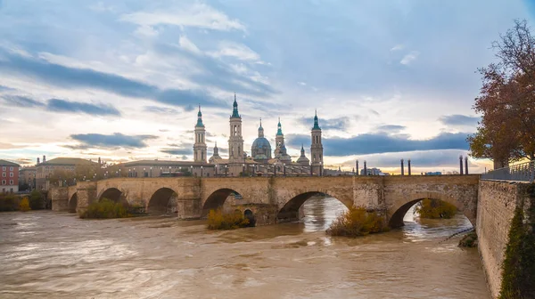 Gün batımında Zaragoza şehrindeki Ebro nehri üzerindeki Bazilika De Nuestra Senora del Pilar 'ın yanındaki taş köprü. İspanya