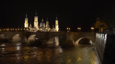 Aragon 'un Zaragoza kentindeki Ebro nehrinin üzerindeki Nuestra Seora del Pilar Bazilikası' nın yanındaki taş köprüden bir gece videosu. İspanya, 4k video