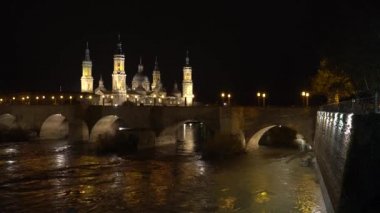 Aragon 'un Zaragoza kentindeki Ebro nehrinin üzerindeki Nuestra Seora del Pilar Bazilikası' nın yanındaki taş köprüden bir gece videosu. İspanya, 4k video