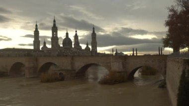 Aragon 'un Zaragoza kentindeki Ebro nehrinin üzerindeki Nuestra Seora del Pilar Bazilikası' nın yanındaki taş köprüden gün batımı. İspanya, 4k video