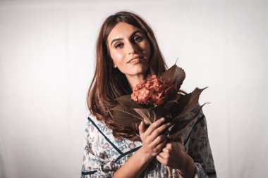 Beyaz arka planda klasik çiçekli bir elbise giyen esmer, beyaz bir kadın. Elinde kırmızı bir çiçekle güzel bir bakışla portre.
