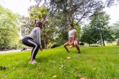 Latin kız yeşil bir parkta spor yapıyor, bayan öğrencilere ağırlık egzersizi öğretiyor.