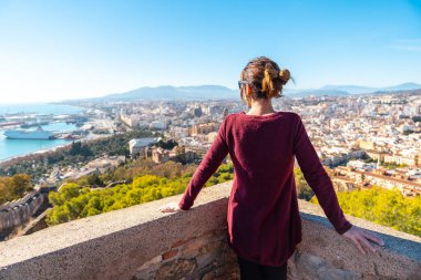 A young woman looking at the city from the wall of the Gibralfaro Castle in the city of Malaga, Andalusia. Spain