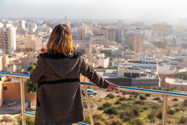 A young tourist girl looking at the city from the viewpoint of Cerro San Cristobal in the city of Almeria, Andalucia. Spain. Costa del sol in the mediterranean sea