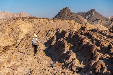 Endülüs 'ün Almerya bölgesindeki Tabernas çölünde Colas de Dragon manzaralarını ziyaret eden şapkalı genç bir yürüyüşçü kız. Çölde yolculuk, yaşam tarzı.