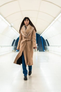 Kışın elinde ceketle metroya giren esmer bir kız pozu. Güzel Kafkasyalı tünelde yürüyor