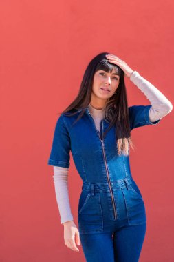 Kot elbise içinde gülümseyen esmer bir kız pozu. Kırmızı arka planda güzel bir beyaz poz