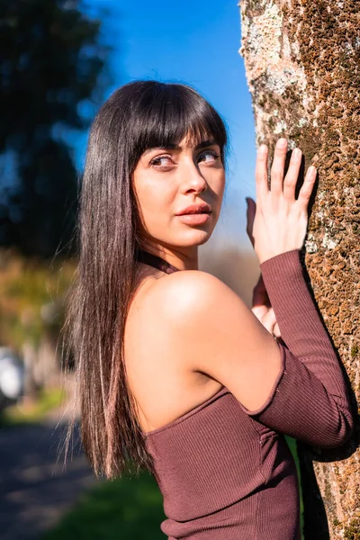 春天的生活方式一个黑发模特儿站在公园里的一棵树上 身穿棕色连衣裙 向左边看去 — 图库照片