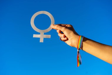 Mavi gökyüzü arka planında feminizmden yana kadın sembolü olan bir kadın eli, kadınlardan yana savaşan, kadın gücü, LGTB bayrağı