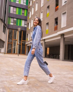 Siyah çantalı, maymun kovboylu, beyaz bir kız. Tatilde şehrin tadını çıkarmak, yeşil bir evde yürüyen genç bir kızın yaşam tarzı, şehir fotoğrafları, dikey fotoğraflar.