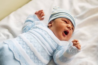 Hastanede yeni doğmuş bir çocuk, hayatının ilk günü, beyaz elbiseli, mavi şapkalı ve beşiğinde yatıyor.