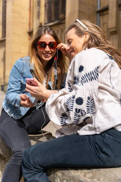 Ascoltando Musica Città Due Amiche Caucasiche Sorridono Condividono Cuffie Ascoltano — Foto Stock