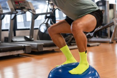 Spor salonunda, kauçuk kürenin ayak bileği için denge egzersizi yapan beyaz bir adamın ayakları. Spor yaparken sağlıklı ve sağlıklı bir yaşam sürüyor.
