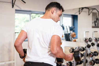 Spor salonunda beyaz tişörtlü, ağırlık kaldıran, sağlıklı ve sağlıklı spor yapan beyaz bir adam.