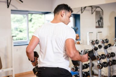 Spor salonunda beyaz tişörtlü, ağırlık kaldıran, sağlıklı ve sağlıklı spor yapan beyaz bir adam.