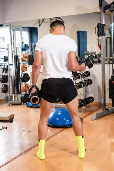 Spor salonunda beyaz tişörtlü, ağırlık kaldıran, sağlıklı ve sağlıklı spor yapan beyaz bir adam.