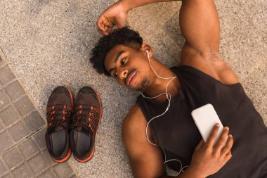 Arap güçlü genç adam şehirde spordan sonra dinleniyor, yere yatıp sola bakıyor.