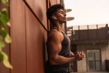 Arap genç adam şehirde spor yapıyor. Duvara yaslanmış kaslarını gösteriyor.