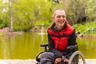 Şehir parkında felçli bir genç adam. Tekerlekli sandalyede oturuyor.