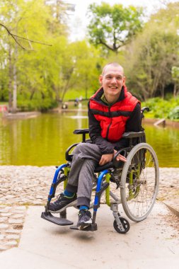 Şehir parkında felçli bir gencin portresi. Tekerlekli sandalyede oturuyor.