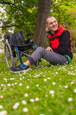 Felç olmuş genç bir adamın portresi tekerlekli sandalyenin yanında oturan papatya çiçekleri, doğada gülümseyen, dikey bir fotoğraf.