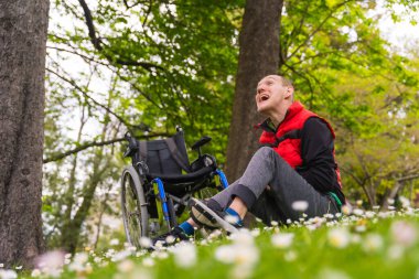 Felç olmuş genç bir adamın portresi. Tekerlekli sandalyenin yanında oturan papatya çiçekli, gülümseyen ve doğanın tadını çıkaran.