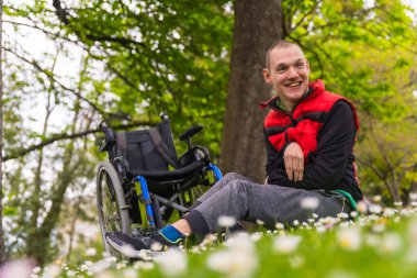 Felç olmuş genç bir adamın portresi. Tekerlekli sandalyenin yanında oturan papatya çiçekli, gülümseyen ve doğanın tadını çıkaran.