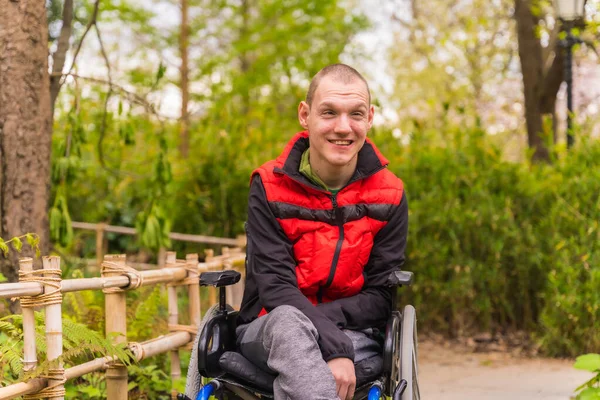Şehir parkında felçli bir gencin portresi. Tekerlekli sandalyede oturmuş gülümsüyor.