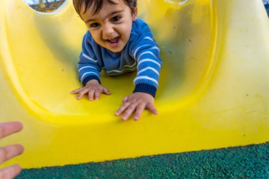 Bir yaşında, beyaz bir çocuk, salıncakta sallanıyor, parkta oynuyor, sarı bir gıcırtıda zıplıyor.