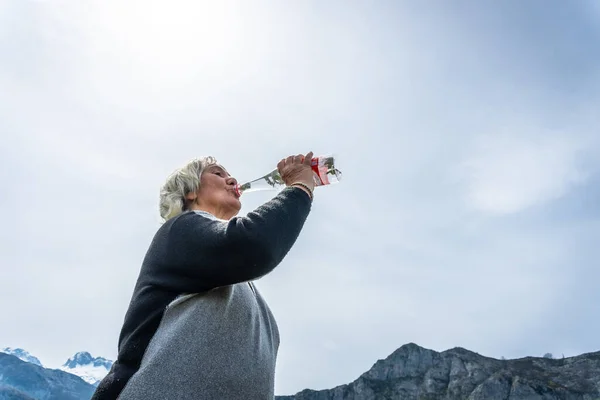 An elderly woman drinking water at Lake Ercina in the Lakes of Covadonga. Asturias. Spain