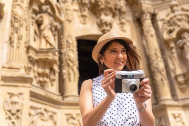 Kiliseyi ziyaret eden ve kamerayla fotoğraf çeken, yaz tatilinin tadını çıkaran, gezgin kadın ve dijital içerik yaratıcısı kavramı ile gülümseyen turist kadın.