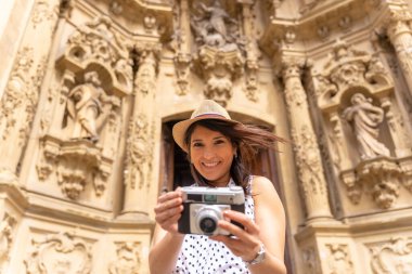 Şehre gelen şapkasıyla gülümseyen ve kamerayla fotoğraf çeken turist kadın yaz tatilinin tadını çıkaran kadın gezgin ve dijital içerik yaratıcısı konsepti