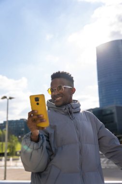 Şehirde telefon ve mavi ceketli zenci bir etnik adam sosyal ağlara bakıyor.