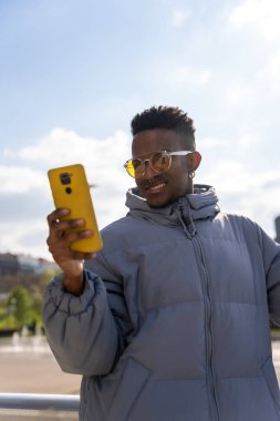 Şehirde telefon ve mavi ceketli zenci bir etnik adam sosyal ağlara bakıyor.