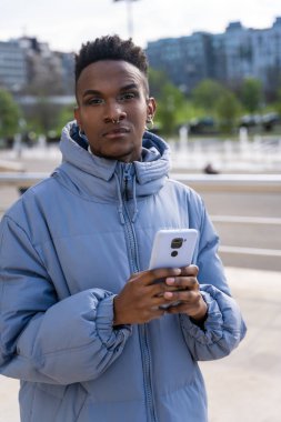 Şehirde telefon ve mavi ceketli siyahi bir etnik adam sosyal ağlara ya da dijital basına bakıyor.