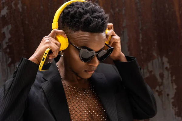 A black ethnic man listening to music wireless yellow headphones, wearing heart sunglasses