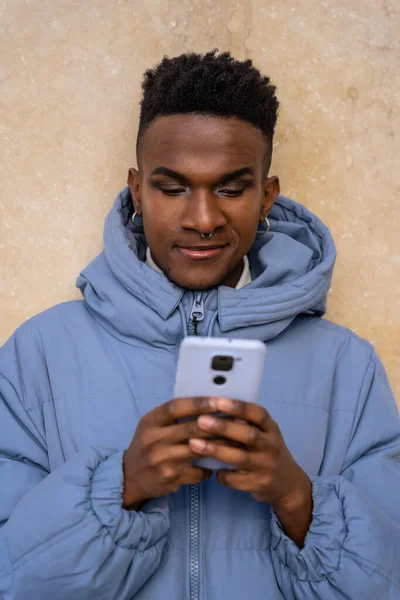 Sarı arka planda telefon ve mavi ceketli siyah kökenli bir adam sosyal ağlara ya da dijital basına bakıyor.