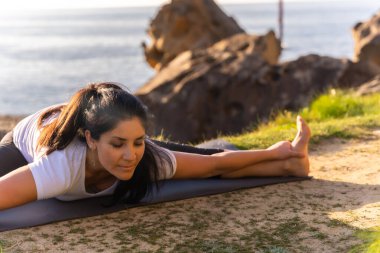 Deniz kenarında yoga egzersizleri yapan, esneme hareketleri yapan bir kadın.