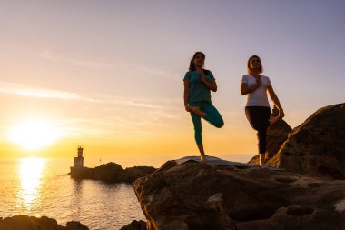 İki kadın, gün batımında deniz kenarında meditasyon ve yoga egzersizleri yapıyorlar. Sağlıklı ve doğa bilimci bir yaşam sürüyorlar.