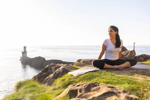 Deniz kenarında yoga egzersizleri yapan bir kadın, ardha padmasana.
