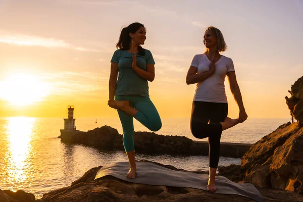 İki kadın, gün batımında deniz kenarında meditasyon ve yoga egzersizleri yapıyorlar. Sağlıklı ve doğa bilimci bir yaşam sürüyorlar.