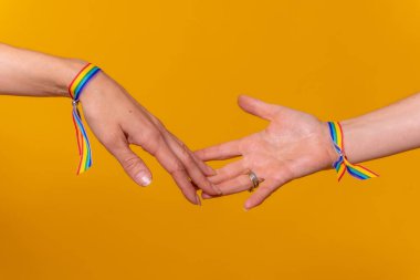 El ele tutuşan iki kadının elleri, sarı arka planda LGBT konsepti, birkaç lezbiyen kız.