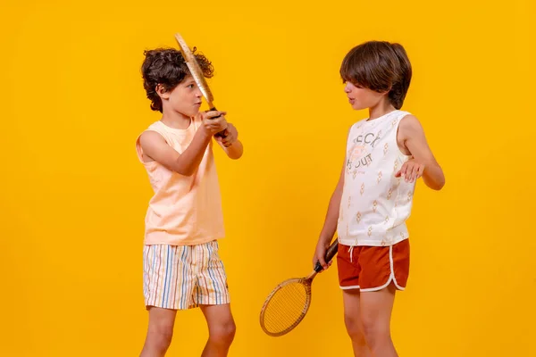 Two brothers playing tennis and having fun on summer vacation, yellow background
