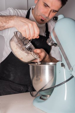 Evde kırmızı kadife kek pişiren bir fırıncı ekmek makinesine un ve maya koyarak kakao tozu hazırlıyor, evde çalışıyor.