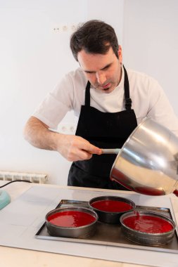 Bir fırıncı evde kırmızı kadife kek pişiriyor, pastayı fırına koymadan önce kalıba ekliyor, evde çalışıyor.