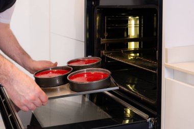Evde kırmızı kadife kek pişiren, fırına kırmızı pasta koyan, evde çalışan bir adamın elleri.