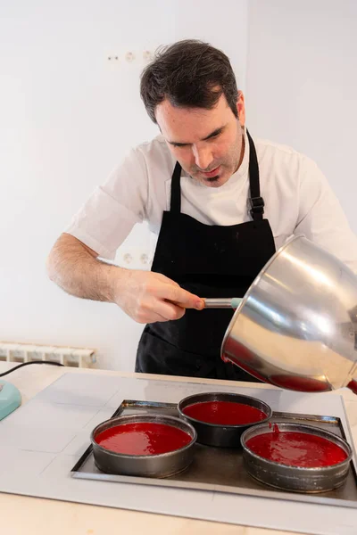 A man baker cooking a red velvet cake at home, adding the cake in the molds before putting it in the oven, work at home